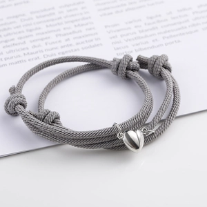 Close-up of gray couple braided bracelets with magnetic heart charm and adjustable knot
