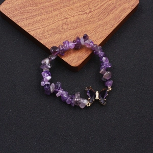 Detail shot of amethyst beaded bracelet with a purple butterfly pendant on wooden tray
