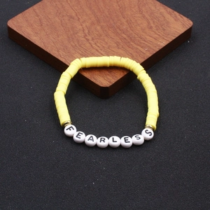 Detailansicht des gelben Heishi-Perlenarmbands mit weißen FEARLESS-Buchstaben und Goldperlen