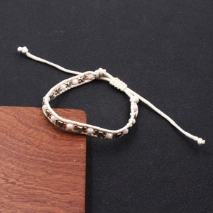 Close-up of bohemian woven bracelet with pink beads and metallic charms on black surface