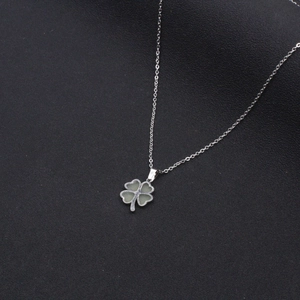 Luminous four-leaf clover pendant necklace with silver chain on black texture background