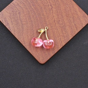 Detailed close-up of a pink acrylic double cherry pendant with golden leaf clasp