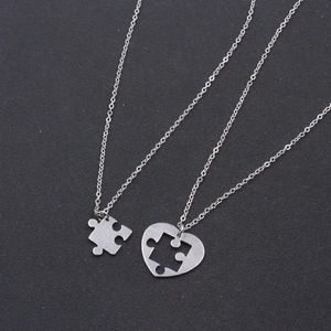 Detail of silver heart-shaped puzzle pieces necklace set for couples on dark background