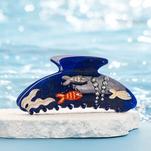Vue détaillée d'une pince à cheveux motif poisson avec strass sur fond d'eau bleue