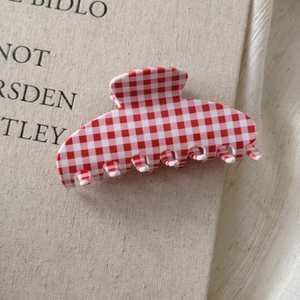 Detailed close-up of red and white gingham checkered acetate hair claw clip on book