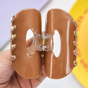 Detail of a large brown hair claw clip with unique oval cutout and striped accents