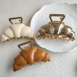 Drei Haarklammern in Croissant-Form in Creme, Gold und Braun auf weißem Hintergrund