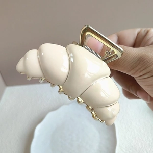 Detaillierte Nahaufnahme einer cremefarbenen Croissant-Haarklammer mit goldener Metallfeder