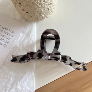 Detailed macro view of an acetate bow claw clip with marble texture and gold lettering