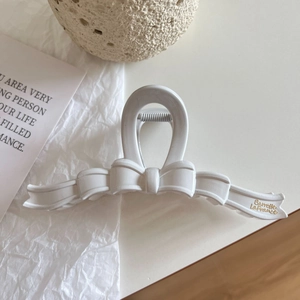 Detail of a creamy white bow hair claw clip with golden text on a textured surface