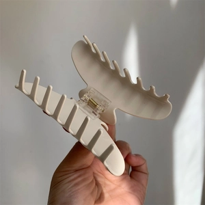 Detail of a cream-colored matte hair claw clip with cross-teeth and gold metal spring