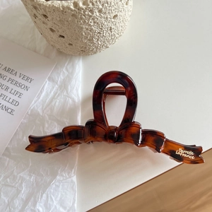 Close-up of tortoise shell bow hair claw clip with golden branding and sturdy metal spring