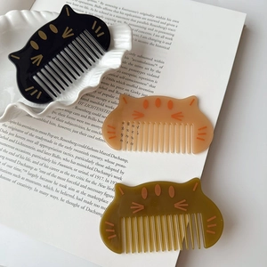 Three cute cat-shaped hair combs in black, amber, and olive green on a white plate