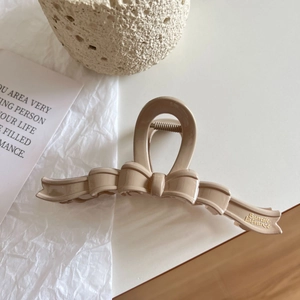 Detail of large beige ribbon-shaped shark hair clip with gold lettering on a textured card