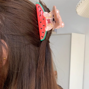 Detail view of a bear and watermelon hair claw clip styling a long hair bun from the side