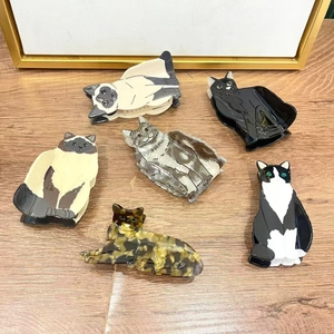 Detailed view of six acetate hair clips in various cat patterns on a wooden surface
