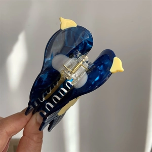 Macro detail of bird-shaped blue acetate hair claw clip with golden metal spring