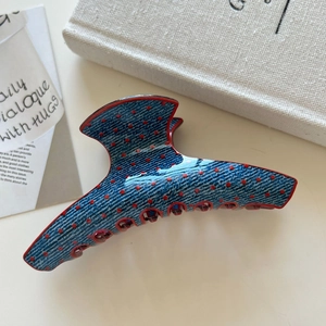 Detail view of large blue denim texture hair claw with red polka dots and red teeth