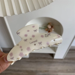 Gros plan d'une pince à cheveux crème avec motifs floraux mauves et strass brillants
