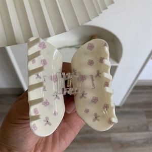 Détail d'une pince à cheveux crème avec des motifs de fleurs roses et de nœuds violets