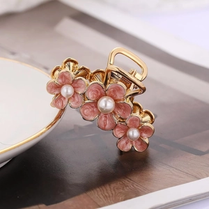 Detail of a golden alloy flower hair claw with pink enamel petals and white pearls