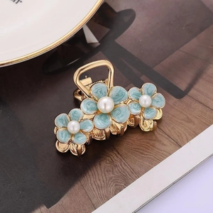 Elegant gold flower hair claw with blue enamel blossoms and pearls on a magazine