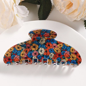 Close-up of floral hair claw clip with colorful daisies on a minimalist stand