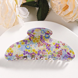 Close-up of a floral print hair claw clip with colorful daisies on a white display tray
