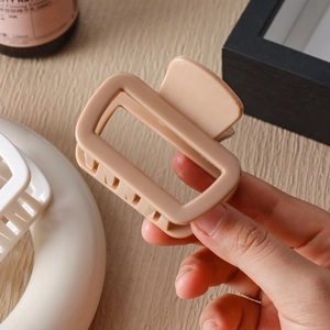 Detail of apricot silicone shark hair claw clip with matte finish held against a wooden background
