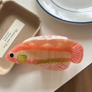 Detail view of the orange and cream fish-shaped hair claw clip with green fin accents