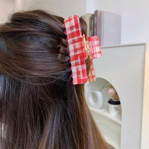 Detail shot of a red and white checkered acetate hair claw clip worn on long brown hair