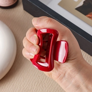 Red silicone hair claw clip with rectangular cutout design held in hand for size comparison
