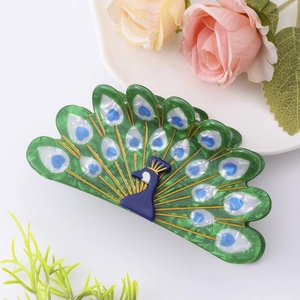 Detail of green peacock acetate hair claw clip with pearlescent finish and blue heart patterns