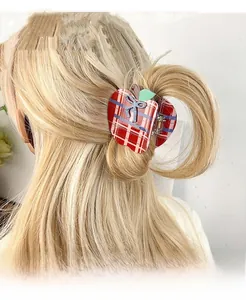 Detail shot of a red plaid apple-shaped hair claw with green leaf and blue bow on dark hair