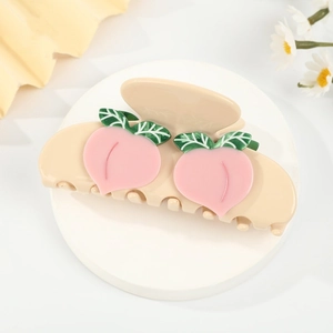 Detail of a creamy peach hair claw clip featuring pink fruits and green leaf accents
