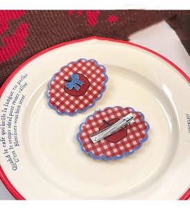 Detail of red and white plaid hair clips with apple and bow designs on a porcelain plate