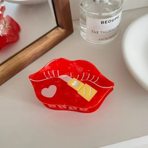 Detail showing red lip-shaped acetate hair claw clip with lipstick and heart patterns