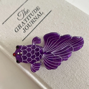 Detail view of purple goldfish hair claw clip with rhinestones on a gratitude journal