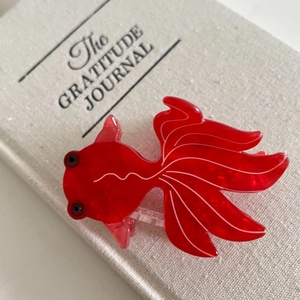 Detailed macro shot of red goldfish hair claw clip with transparent acetate texture on a book
