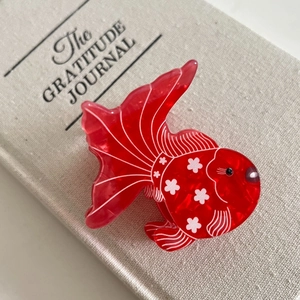 Close-up of a goldfish-shaped red acetate hair claw with delicate white floral patterns