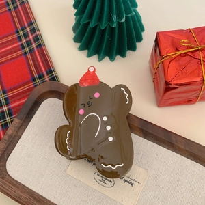 Close-up of a gingerbread man hair claw clip with a red hat on a festive wooden tray