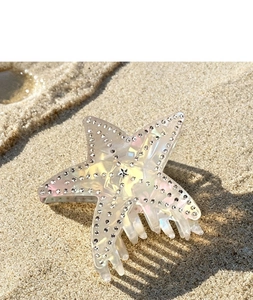 Detailed macro of a starfish-shaped hair claw with sparkling rhinestones on beach sand