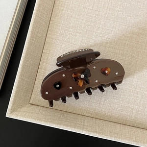 Close-up of brown acetate hair claw with rhinestone bow and heart patterns in a tray