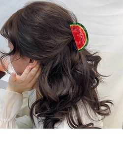 Détail d'une pince à cheveux motif pastèque stylisée sur des cheveux bruns ondulés