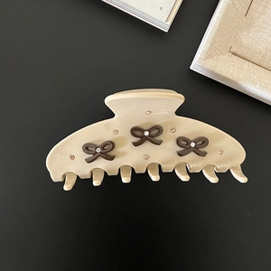 Close-up of cream acetate hair claw with brown rhinestone bows and polished finish
