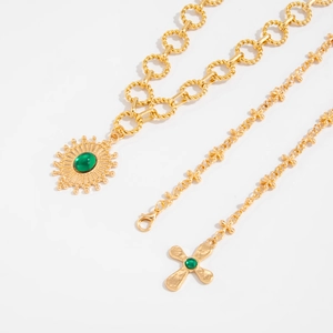 Détail de colliers superposés dorés avec pendentifs croix et soleil et pierres vertes