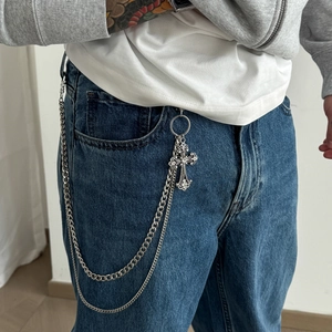 Detail of silver layered metal pants chain featuring a punk cross pendant on blue jeans