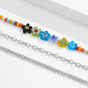 Collier multi-rangs avec perles colorées, chaîne argentée et fleurs sur socle blanc