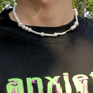 Detailopname van een witte parelketting met gouden kralen op een mannelijk model