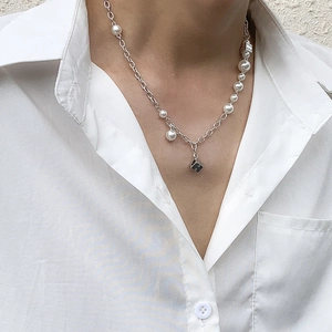 Detail of necklace with white pearls, silver chain, and unique dice pendants on a model